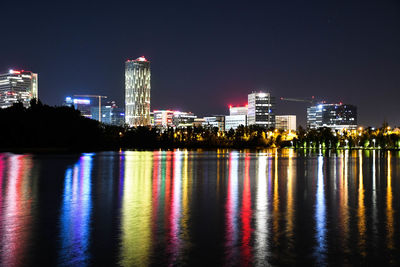 Illuminated buildings by river against sky at night