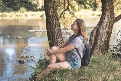 Side view of woman sitting by water stream