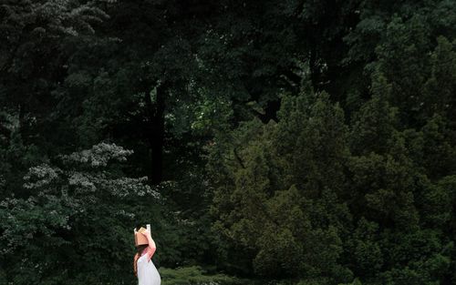 Side view of woman carrying box on head while standing against tree