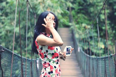 Young woman using mobile phone while standing on tree