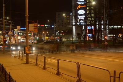 Illuminated street by buildings in city at night