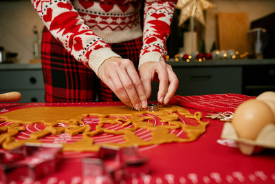Woman cutting christmas cookies from dough on red mat