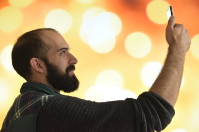 Profile view of man taking selfie while standing against illuminated lights at night