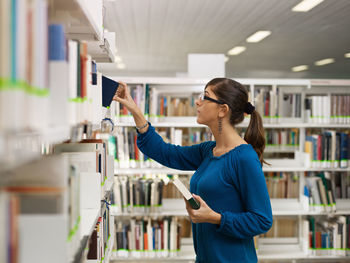 Side view of woman searching book on shelf in library