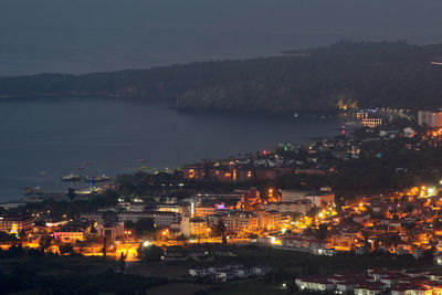 High angle view of illuminated buildings by sea against sky at night