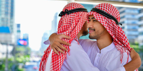 Close-up of businessmen in traditional clothing embracing against buildings