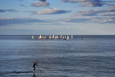 Side view of man paddleboarding in sea against cloudy sky