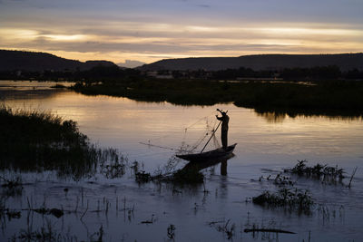 Silhouette man fishing in lake against sky during sunset