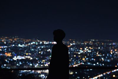 Rear view of silhouette man looking at illuminated city buildings