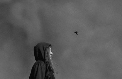 Low angle view of airplane flying over woman against sky