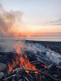 Bonfire by sea against sky during sunset