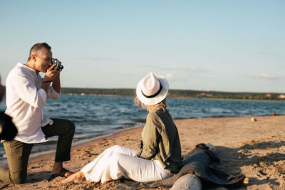 An adult man takes a retro camera of his woman on the beach