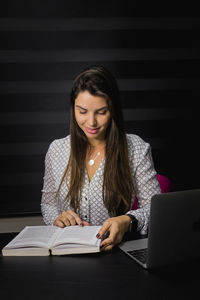 Young woman using mobile phone while sitting on book