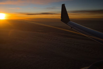 Airplane flying over land against sky during sunset