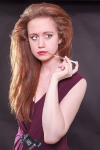 Portrait of young woman smoking over black background