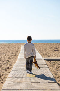 Little kid on a beach walkway with a dinosaur in his hands