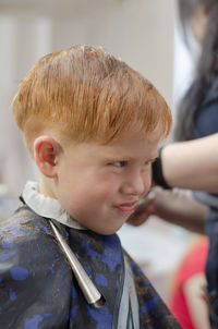 Little red-haired boy in the barbershop grimaces. boy 4 years old in a hairdresser