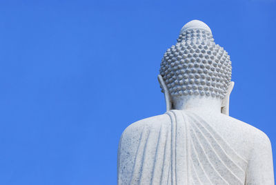 Low angle view of buddha statue against clear blue sky