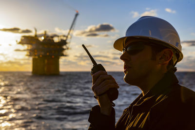 Portrait of man holding smart phone by sea against sky