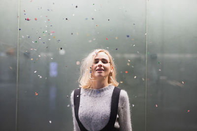 Portrait of smiling woman with blond hair standing against wall