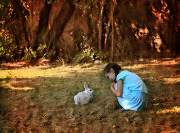 Cute girl with rabbit crouching on field