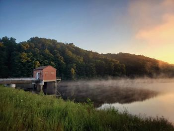 Scenic view of lake by building against sky at dawn