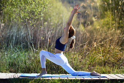 Side view of mid adult woman with arms raised exercising on boardwalk at park