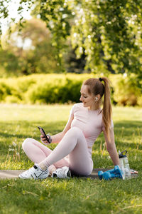 Sports girl listens to music in headphones while sitting on a fitness mat