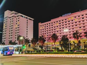 Illuminated buildings by road against sky in city at night