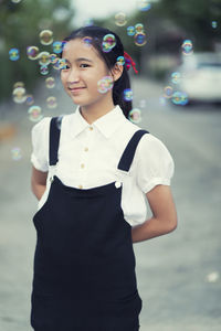 Portrait of smiling teenage girl standing amidst bubbles outdoors