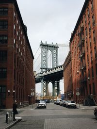 Street amidst buildings by manhattan bridge against sky