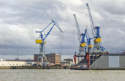 Cranes at commercial dock against sky