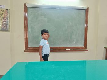 Full length of young boy standing by white board 