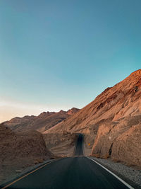 Road leading towards mountains against clear blue sky