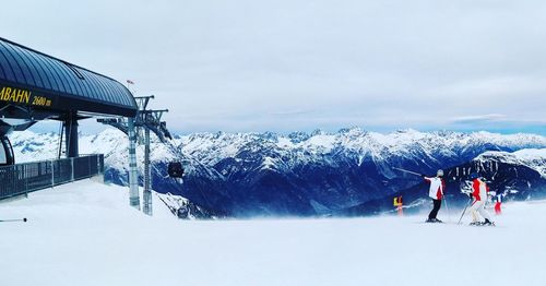 People skiing on snowy field against mountains and sky during winter