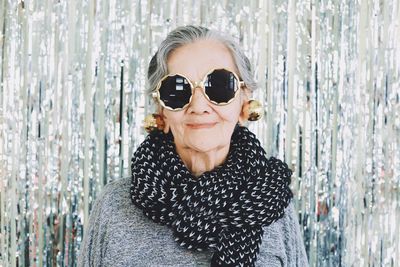 Portrait of smiling woman wearing sunglasses while standing against wall