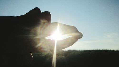 Low angle view of hand against sun during sunset