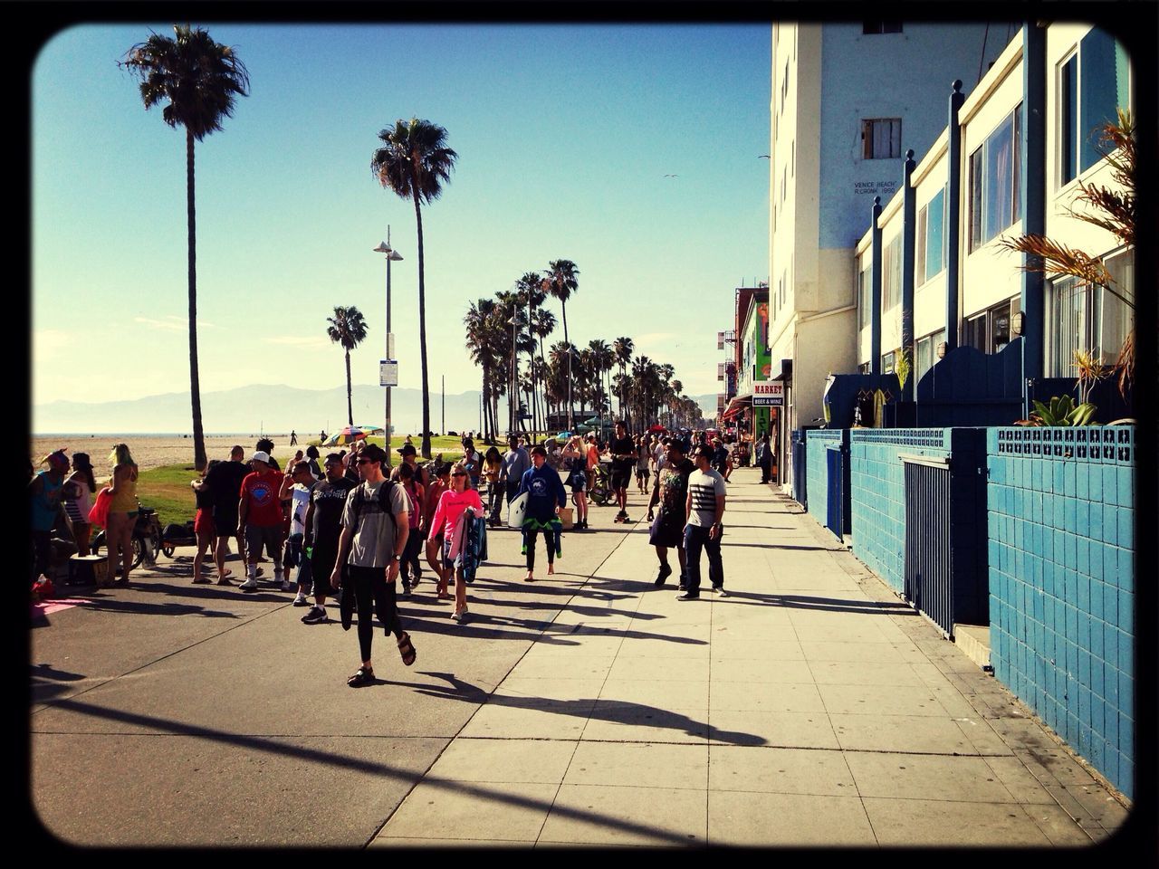 large group of people, transfer print, person, men, lifestyles, tree, building exterior, built structure, walking, architecture, clear sky, auto post production filter, leisure activity, street, city, sunlight, city life, shadow, mixed age range