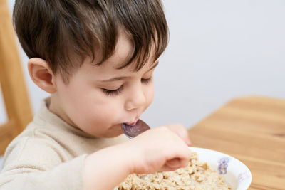 Little boy eating oatmeal for breakfast in the kitchen