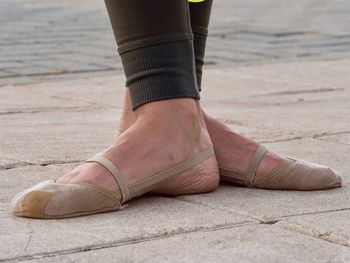 Low section of woman in ballet shoes standing on paving street