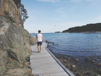 Rear view of woman standing on shore against sky