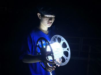 Midsection of man holding illuminated lighting equipment against black background