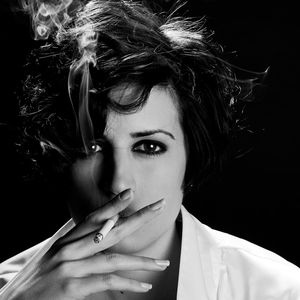 Close-up portrait of young woman smoking cigarette against black background