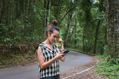 Young woman look at phone and thinking, confuse, standing beside a road 