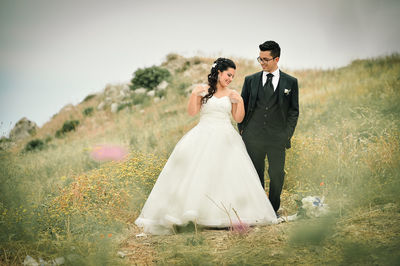 Newlywed couple standing on grassy field against sky
