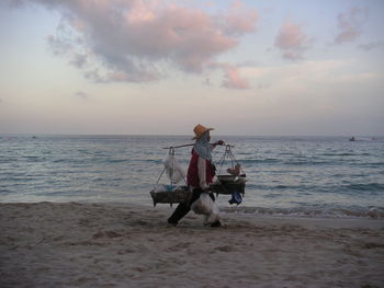 Man riding horse on beach against sky during sunset