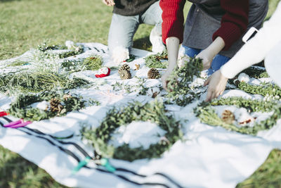 Midsection of women making wreath on fabric at grassy field during christmas