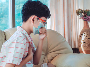 Close-up of boy wearing mask sitting on sofa