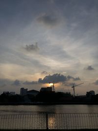 Silhouette factory by sea against sky during sunset