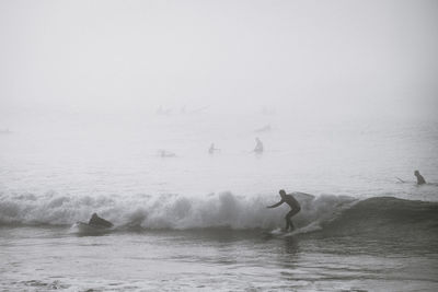 People surfboarding in sea during foggy weather